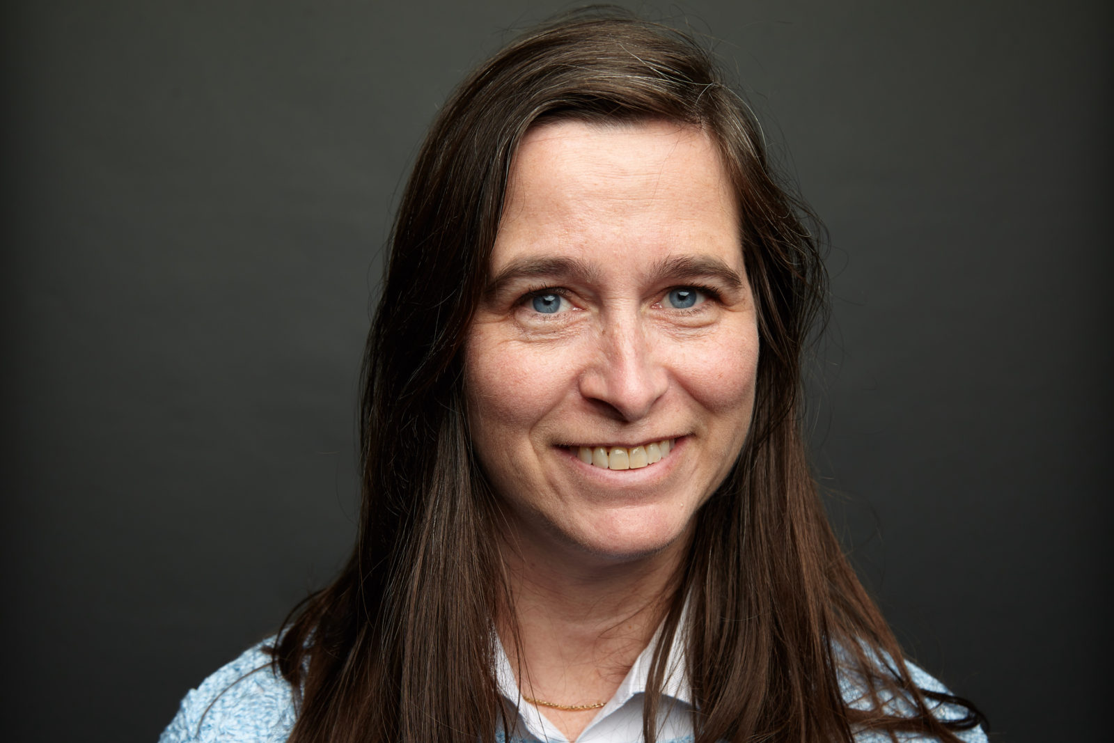 Portrait of a smiling woman with long brown hair against a dark background.